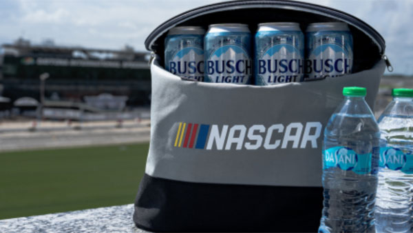 NASCAR-branded cooler filled with cans of Busch Light, with two bottles of water beside it and Talladega Superspeedway in the background.