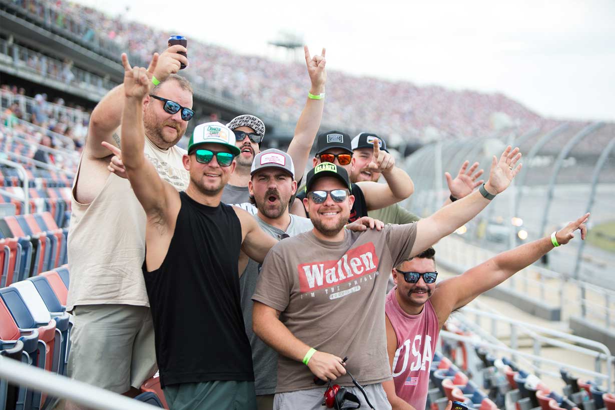 Group of NASCAR fans cheering and posing together in the grandstands at Talladega Superspeedway.